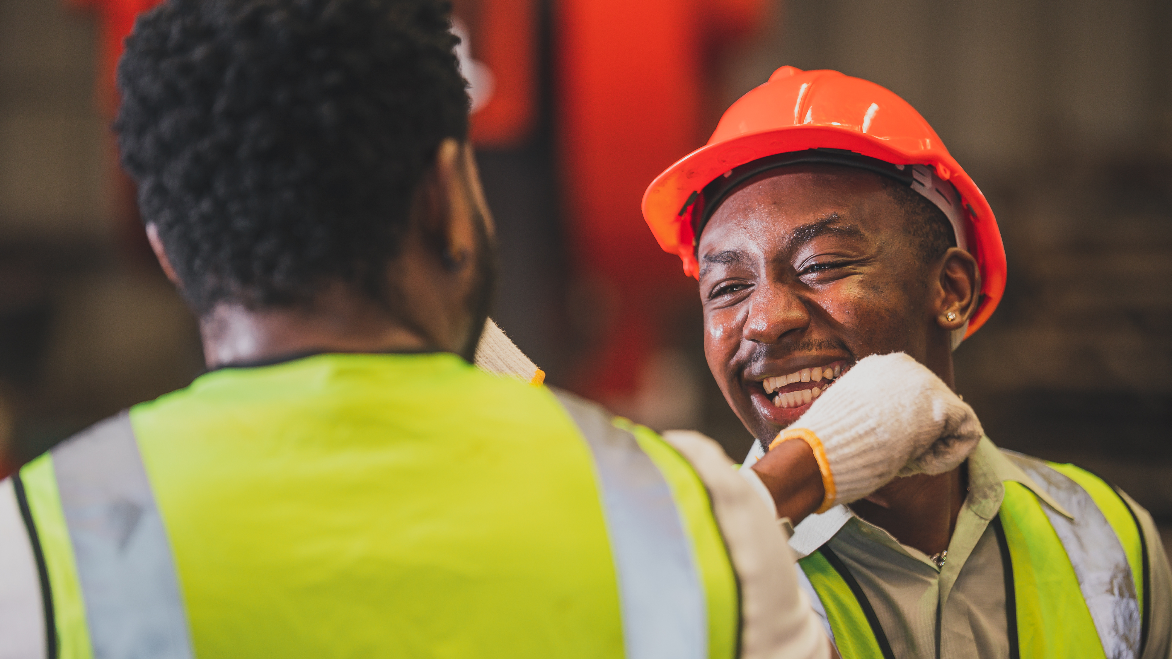 two industrial workers in red hardhats bumping elbows to celebrate a completed task in warehouse distribution center