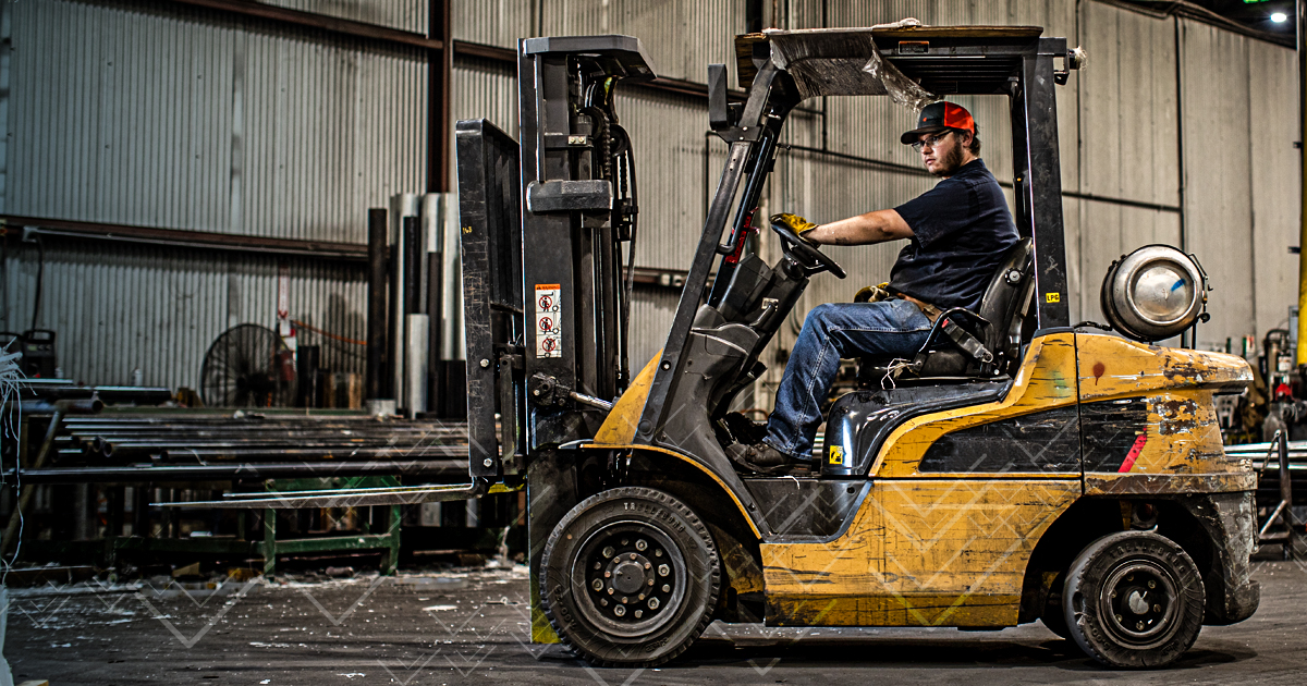 worker at manufacturing facility operating a forklift in order to move metal pipes and rods